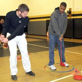Wayne Ogle, left, PGA Professional at Sedalia Country Club, offers instruction on a proper swing to Smith-Cotton High School boys basketball Coach Ray Hughes during the SNAG instructional session Feb. 18 in the Sedalia Middle School Gymnasium. SNAG -- Starting New At Golf -- will be introduced as part of physical education courses at all Sedalia 200 schools.