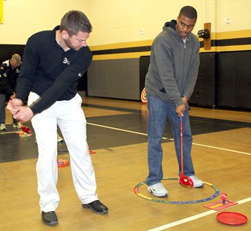 Wayne Ogle, left, PGA Professional at Sedalia Country Club, offers instruction on a proper swing to Smith-Cotton High School boys basketball Coach Ray Hughes during the SNAG instructional session Feb. 18 in the Sedalia Middle School Gymnasium. SNAG -- Starting New At Golf -- will be introduced as part of physical education courses at all Sedalia 200 schools.